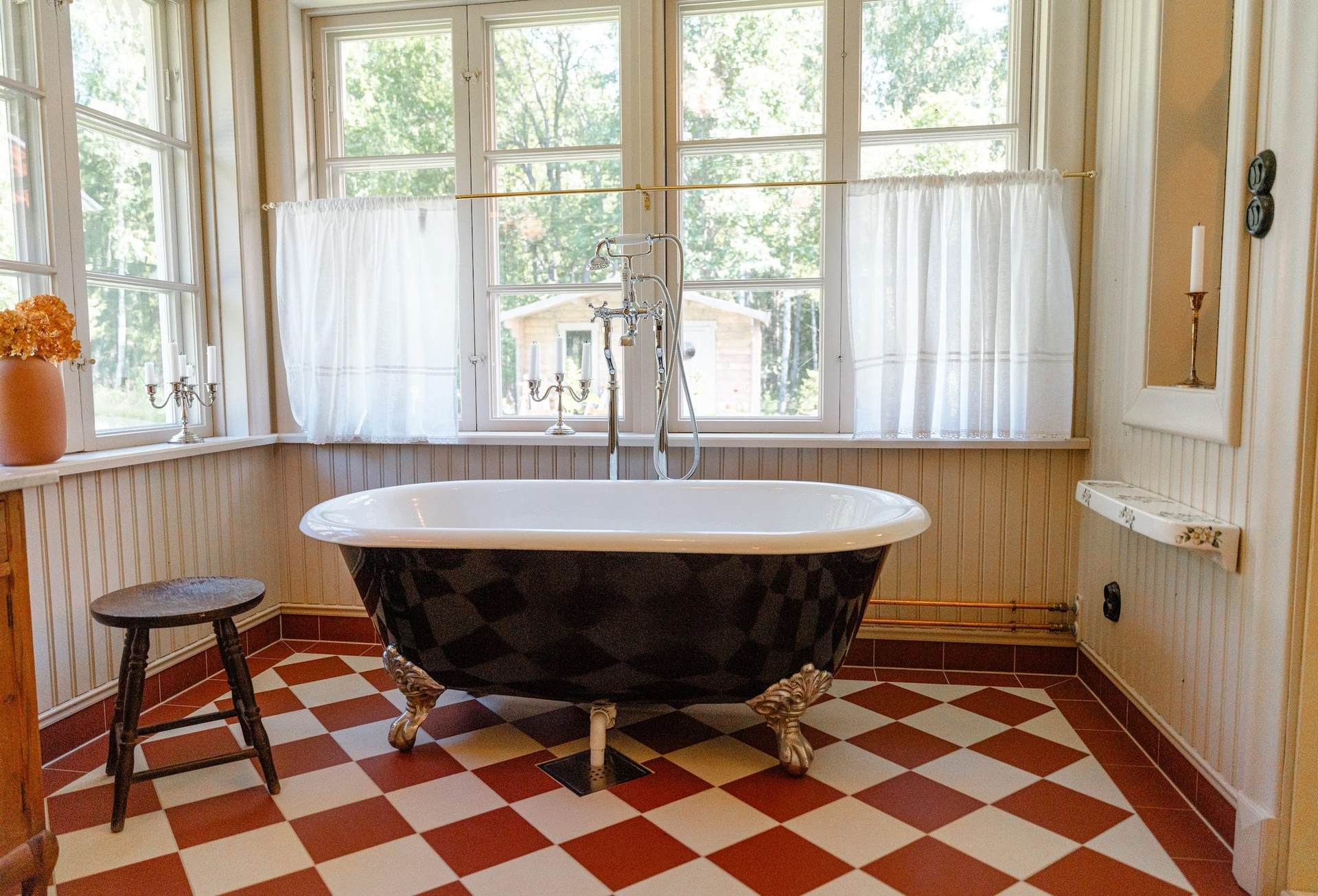 Black clawfoot bath in front of a row of windows on a chequered floor